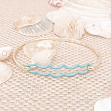 Load image into Gallery viewer, the beach and back double aqua wave tension bangle in gold tone on neutral color woven textured table top with white seashells scattered in the background