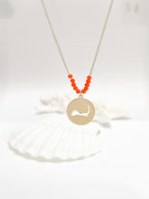 Load image into Gallery viewer, the beach and back cape cod necklace in gold with coral beads at center of chain and coin shape pendant with cutout silhouette of cape cod pictured in front of white seashells on white background
