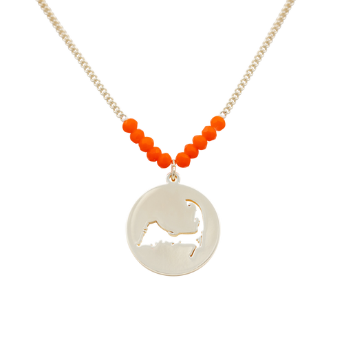 the beach and back cape cod necklace in gold with coral beads at center of chain and coin shape pendant with cutout silhouette of cape cod