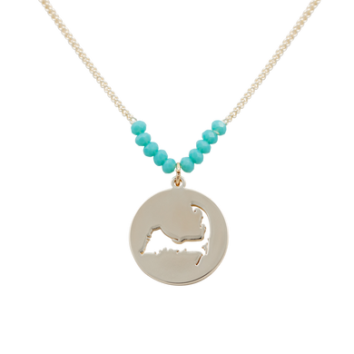 the beach and back cape cod necklace in gold with turquoise beads at center of chain and coin shape pendant with cutout silhouette of cape cod