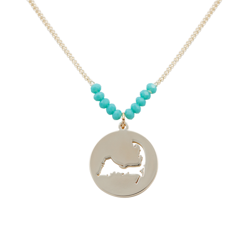 the beach and back cape cod necklace in gold with turquoise beads at center of chain and coin shape pendant with cutout silhouette of cape cod