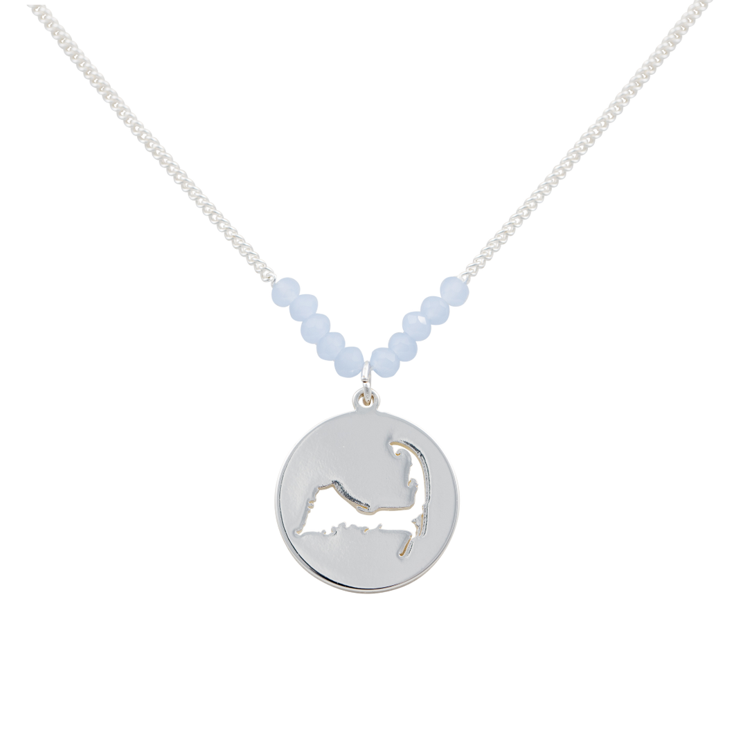 the beach and back cape cod necklace in silver with pale blue beads at center of chain and coin shape pendant with cutout silhouette of cape cod